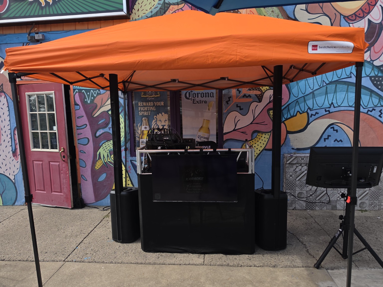 Karaoke and DJ equipment set up outdoors under an orange canopy
