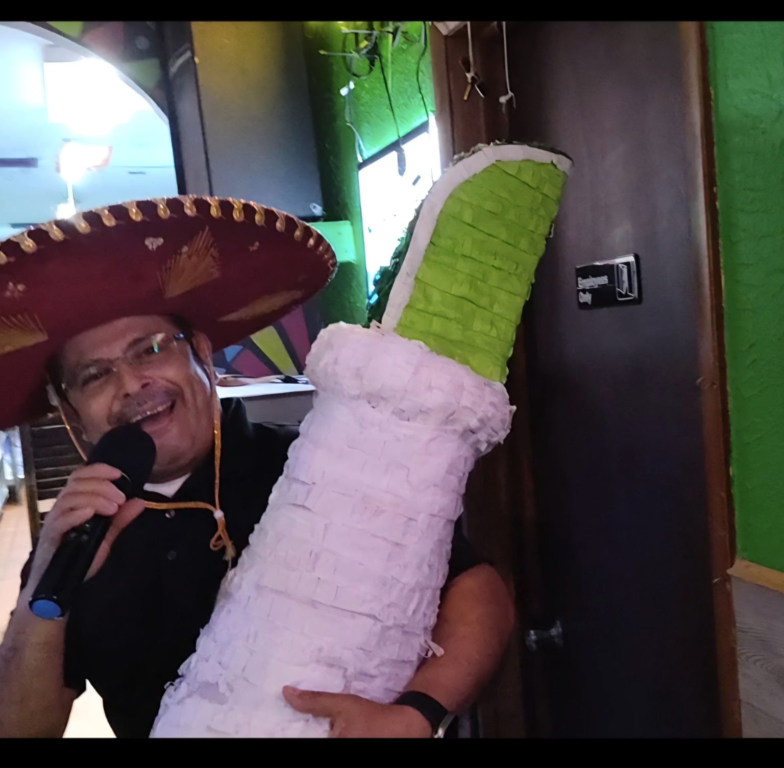 Man in a sombrero singing karaoke beside a festive decoration