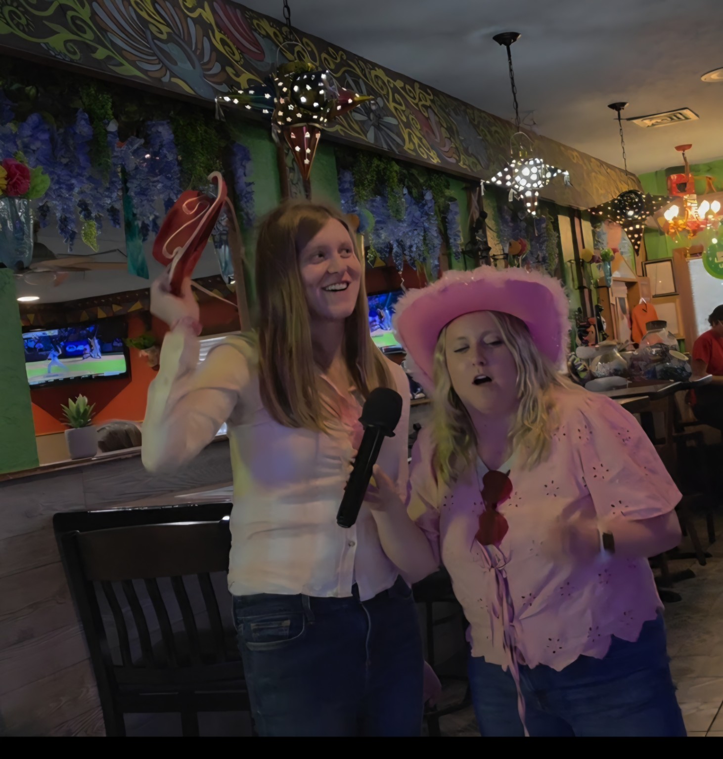 Two women in party hats singing karaoke