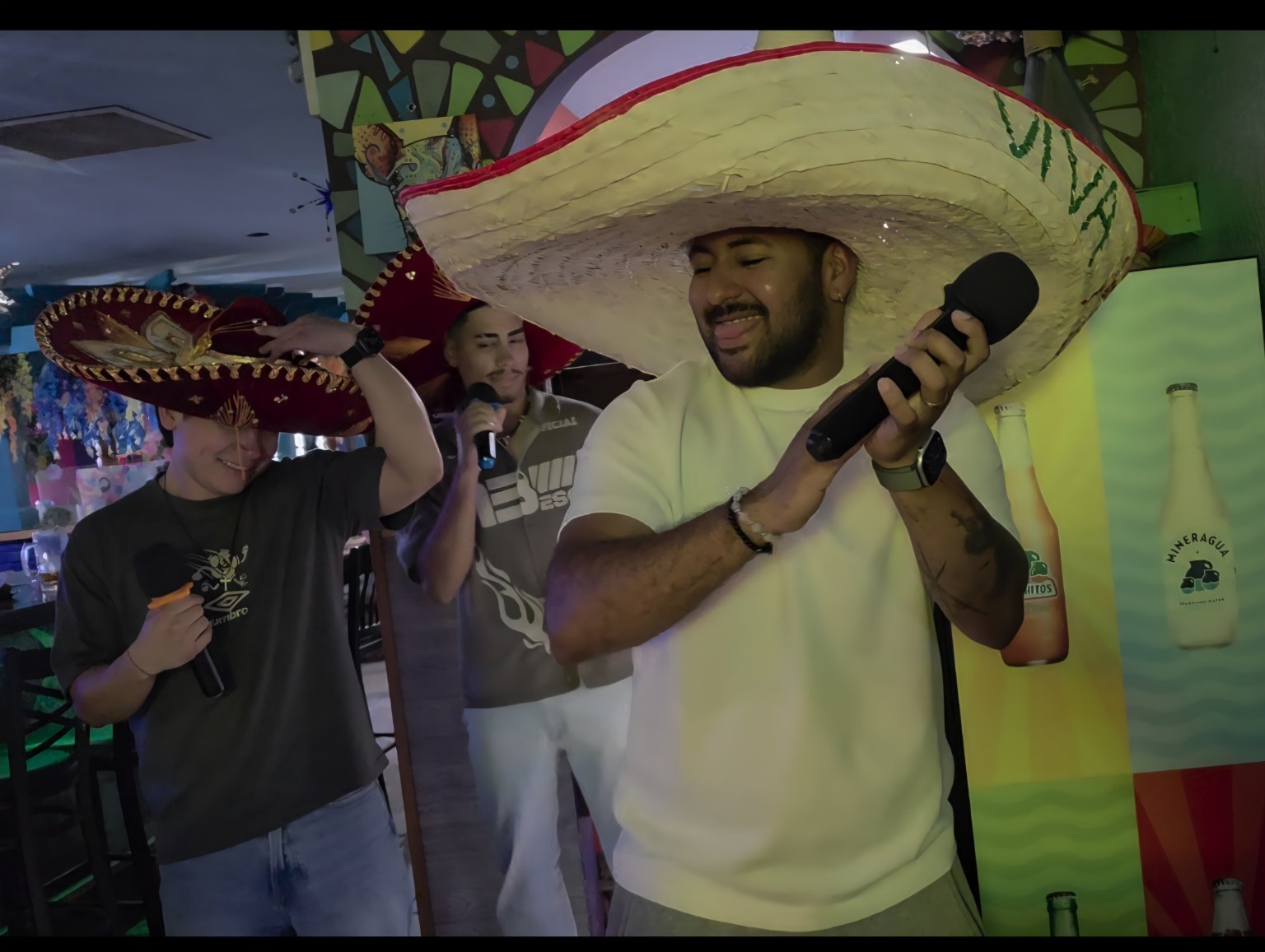 Three friends singing karaoke in sombreros